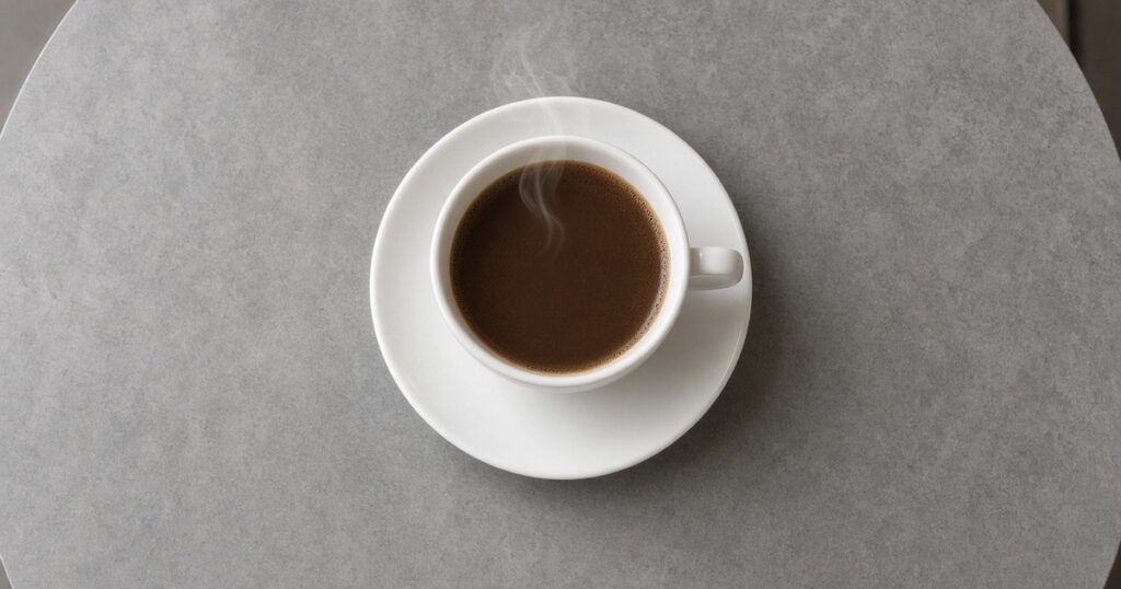 A white coffee cup and saucer with steam on a gray table.