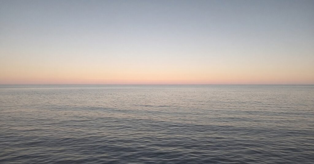 A calm gray sea under a pale dawn sky.