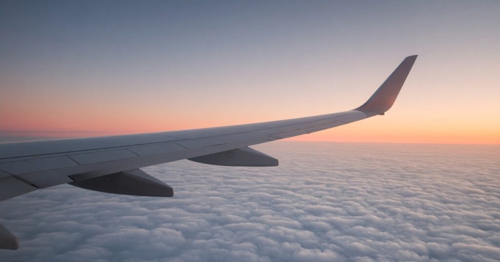 An airliner wing above clouds at sunrise.