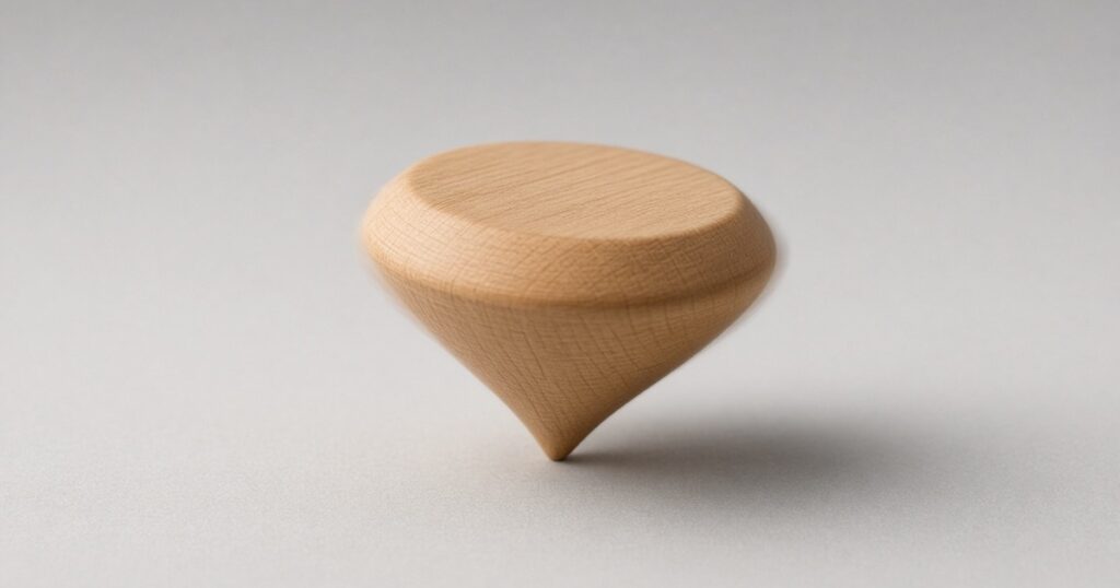 A plain wooden spinning top spins upright on its point, its edge slightly blurred, on a smooth light gray surface.
